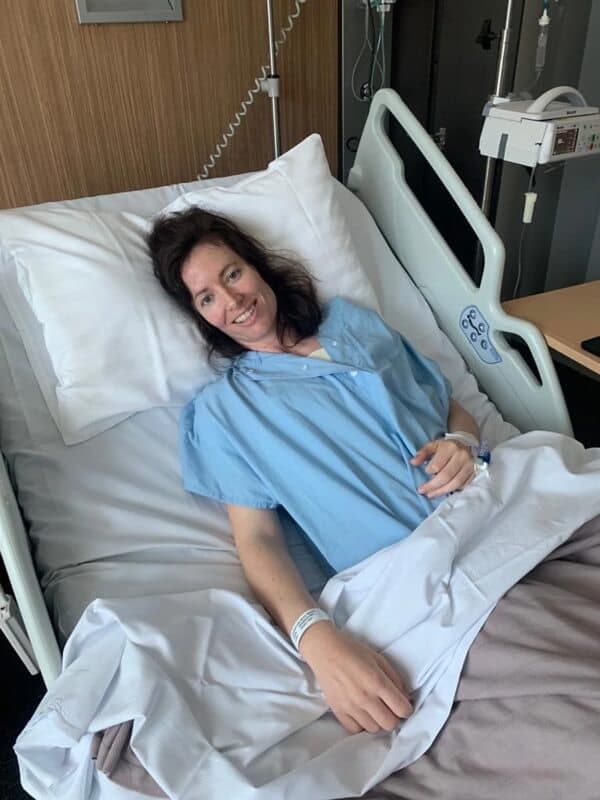 Meryl smiling from a hospital bed in a blue gown